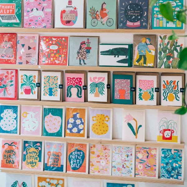 Shelves displaying a variety of colorful greeting cards against a white wall.